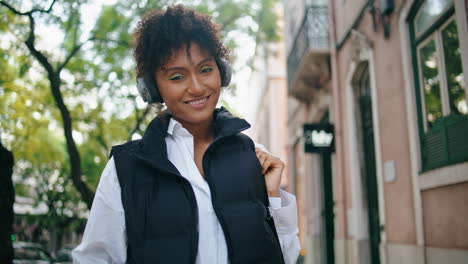 girl tourist walking street in earphones close up. african woman posing vertical