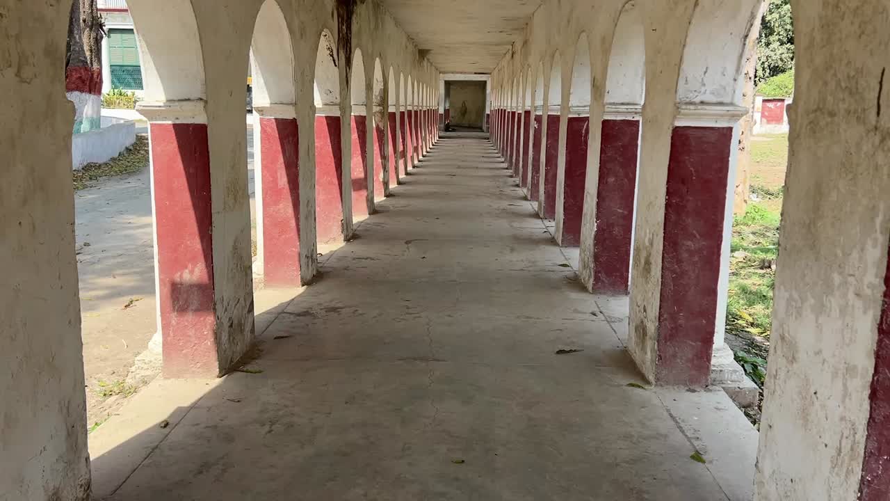Shot of corridor or walkaway with series of repeating painted arched openings on both sides in a jail in India.