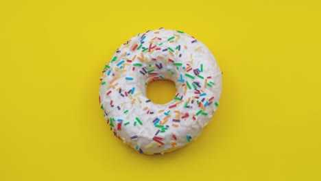 girando un primer plano de una deliciosa rosquilla blanca con salpicaduras coloridas sobre un fondo amarillo.