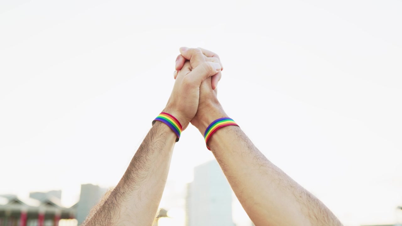 Mani giunte con braccialetti del Pride LGBTQ+.