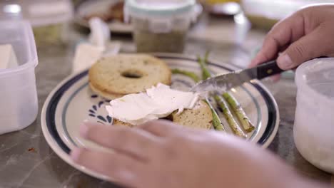 crop woman spreading cream cheese on bun