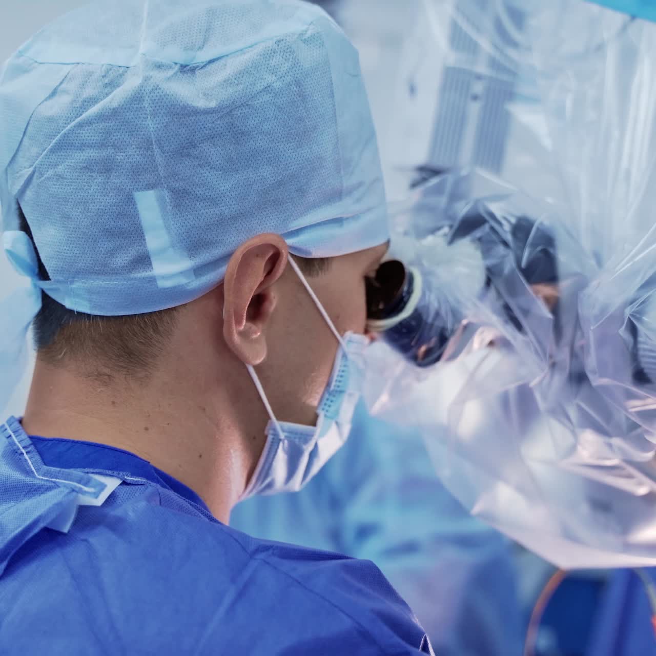 Doctor looks through the microscope. Professional neurosurgeon in medical uniform and mask operates the patient. Close-up.