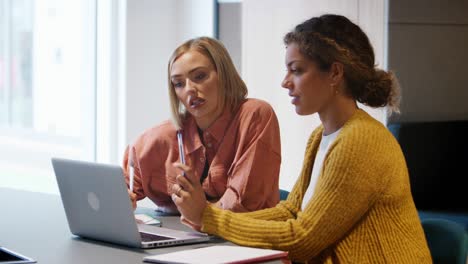 two young female creatives sitting in an office working together, in discussion at a laptop computer, close up