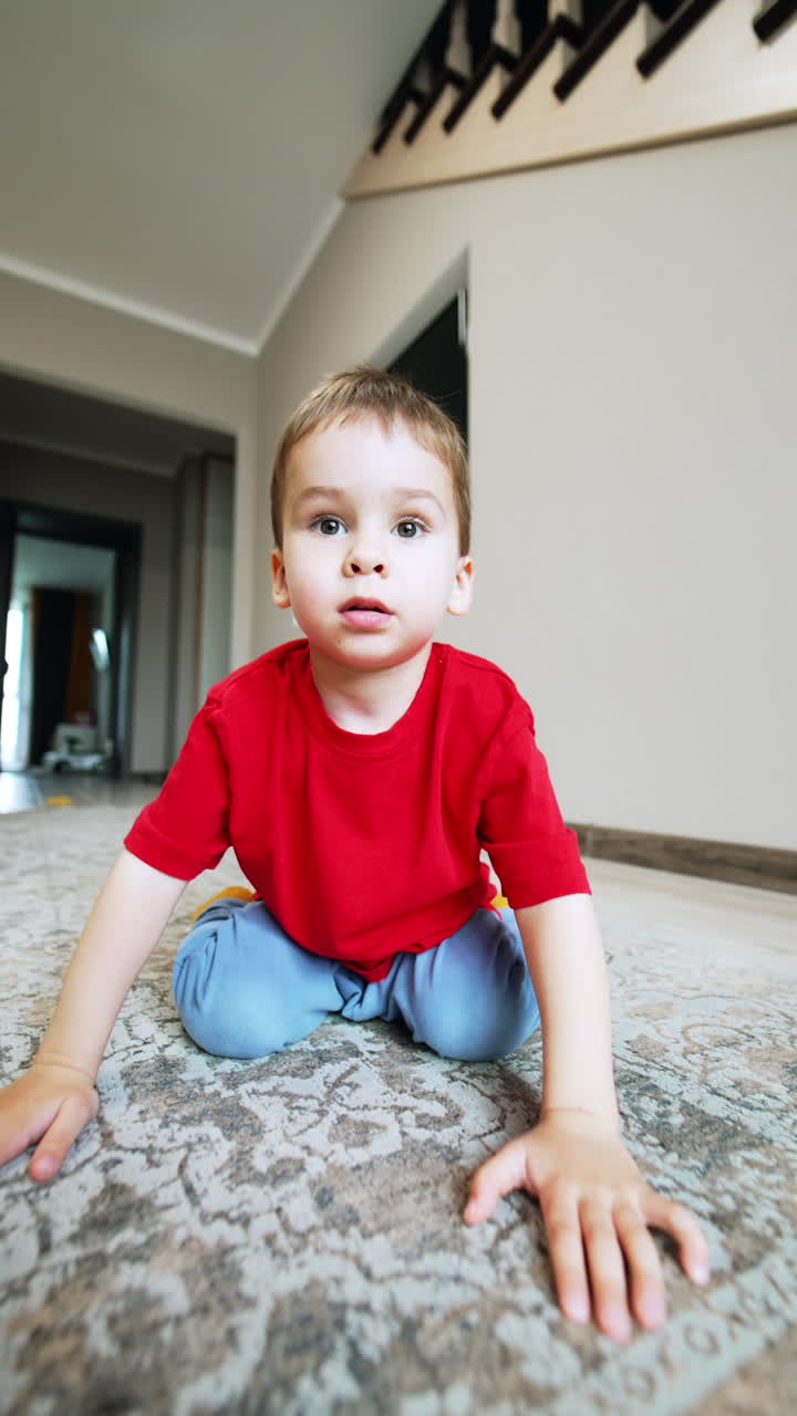 Beautiful Caucasian baby boy sits on the floor looking at camera. Toddler looks calm and then smiles widely. Close up. Vertical video.