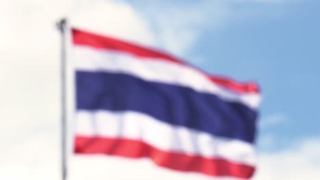 Thailand-national-flag-hoisted-on-a-white-tall-steel-pole-blown-by-the-wind-creating-an-animated-wave-on-a-backdrop-of-a-clear-blue-sky-and-white-clouds