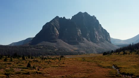 Stunning-aerial-drone-landscape-nature-trucking-right-shot-of-a-large-meadow-with-a-small-stream-with-the-beautiful-Lower-Red-Castle-Lake-and-peak-behind-up-in-the-High-Uinta-national-forest-in-Utah