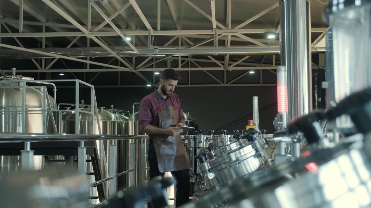 un joven cervecero con un delantal de cuero supervisa el proceso de fermentación de la cerveza en una fábrica de cerveza moderna