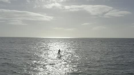 el paddleboarder de pie solitario está recortado en un rayo de sol en el océano picado