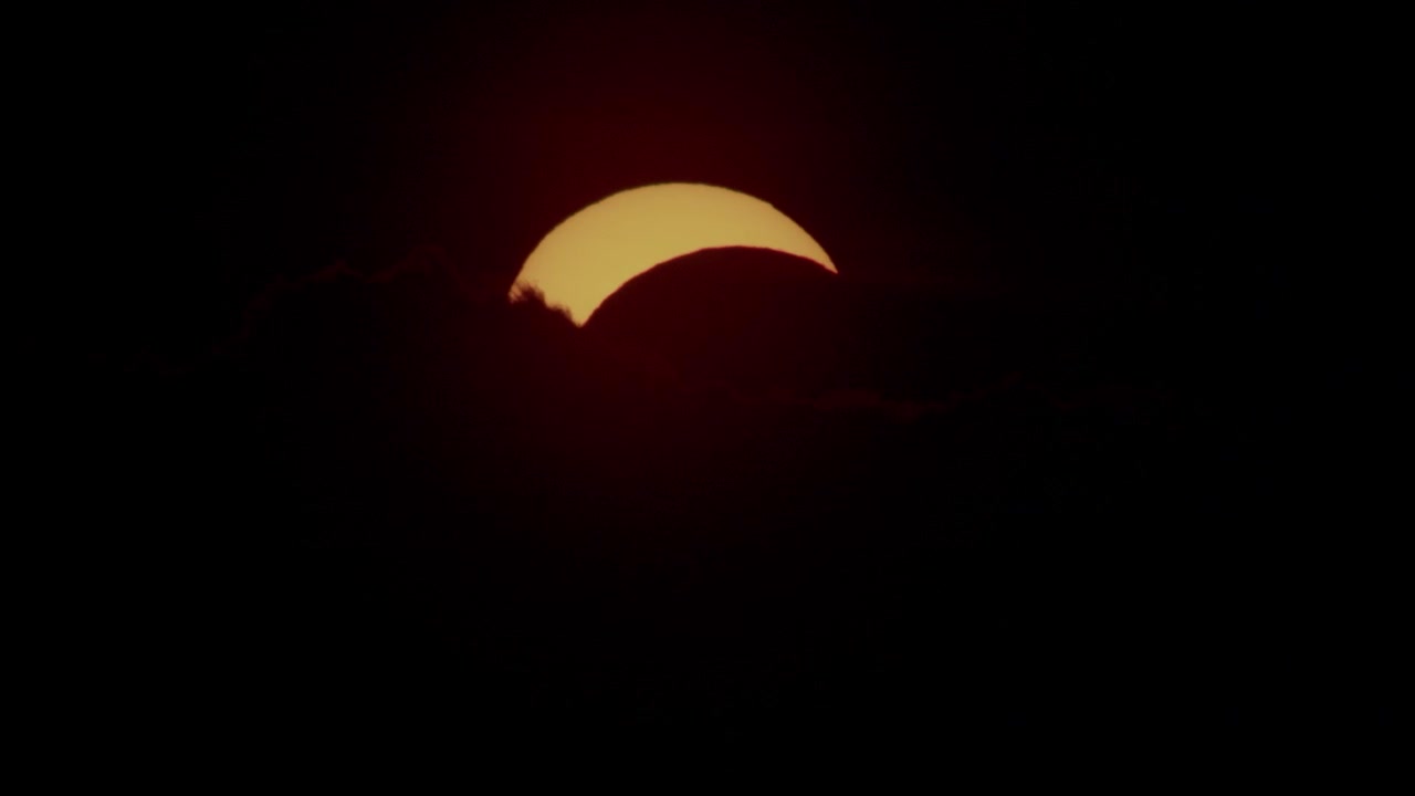Partial solar eclipse through clouds in sunset moment near horizon