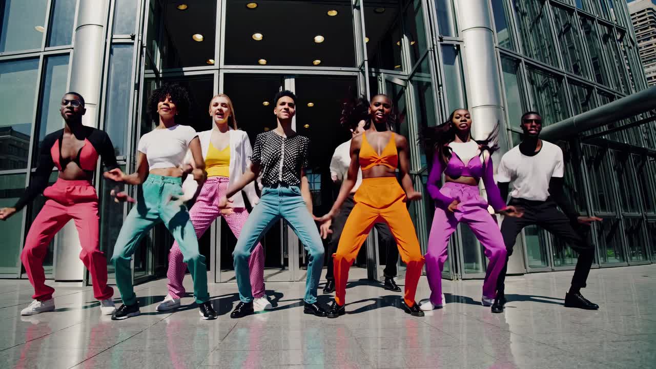 bailarines enérgicos ejecutando coreografías precisas, usando trajes brillantes contra la arquitectura de vidrio moderna, destacando el rendimiento colaborativo y la expresión artística urbana
