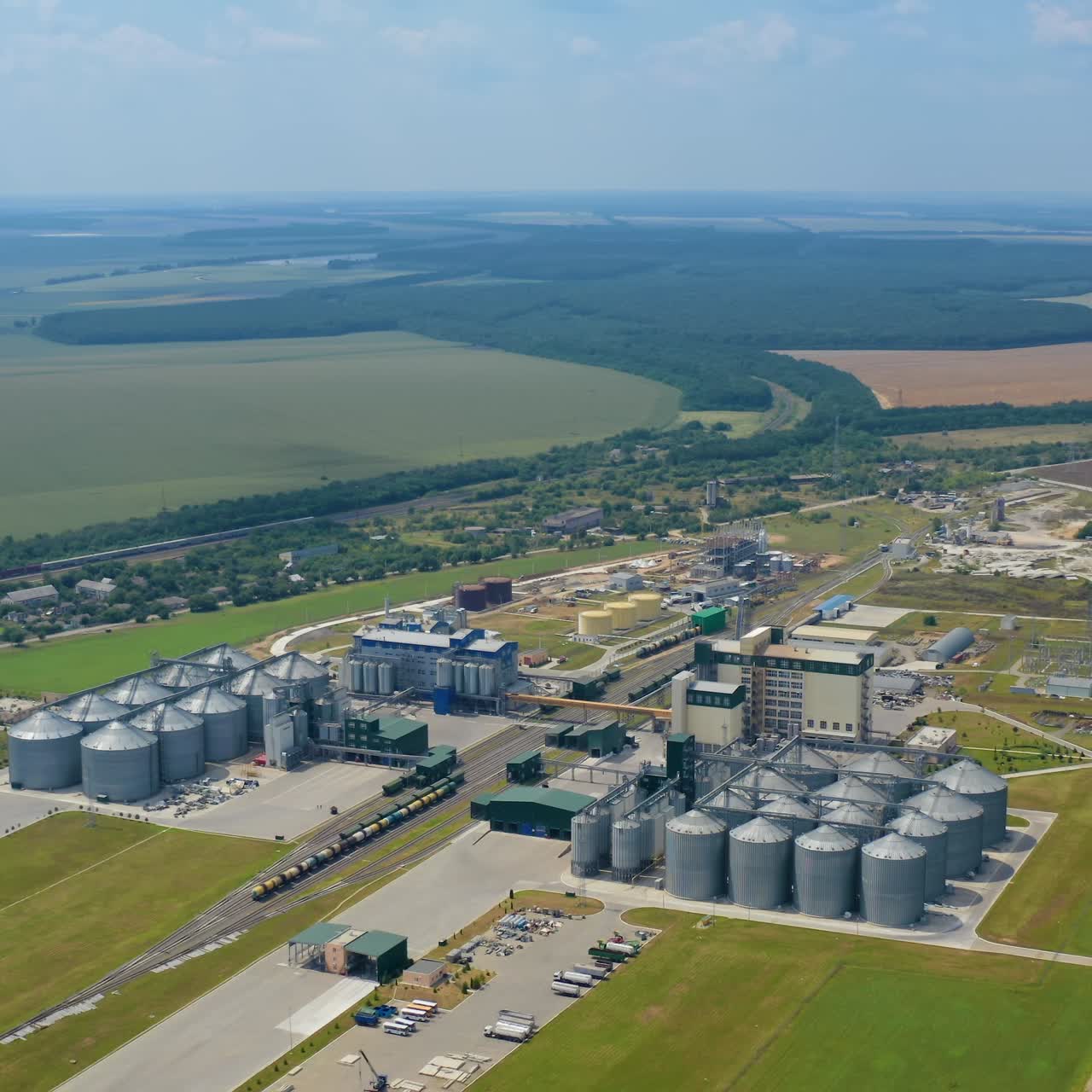 Innovative agriculture factory in nature. Modern grain silos elevators on green field in summer. Steel granary. Aerial view