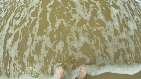 a little wave is coming and is foaming the feet, holiday vibes from a top-down view