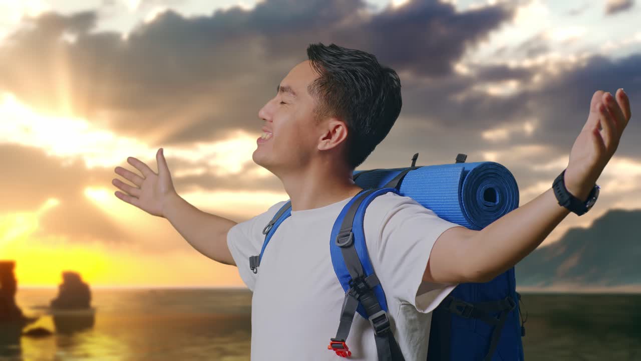 Primo piano laterale di escursionista asiatico con zaino da alpinismo che allarga le braccia e si gode il panorama sulla spiaggia