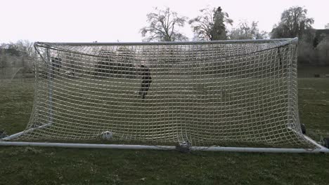 slow motion: a man kicks a soccer ball which slams an icy net of a soccer goal exploding shattered ice into the air-1