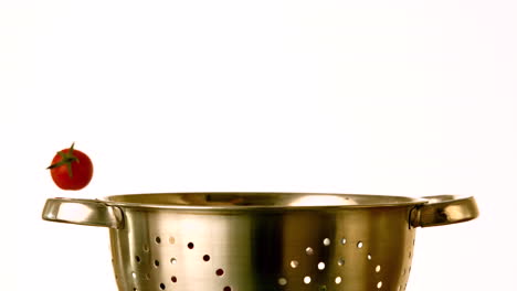 cherry tomatoes falling into colander on white background