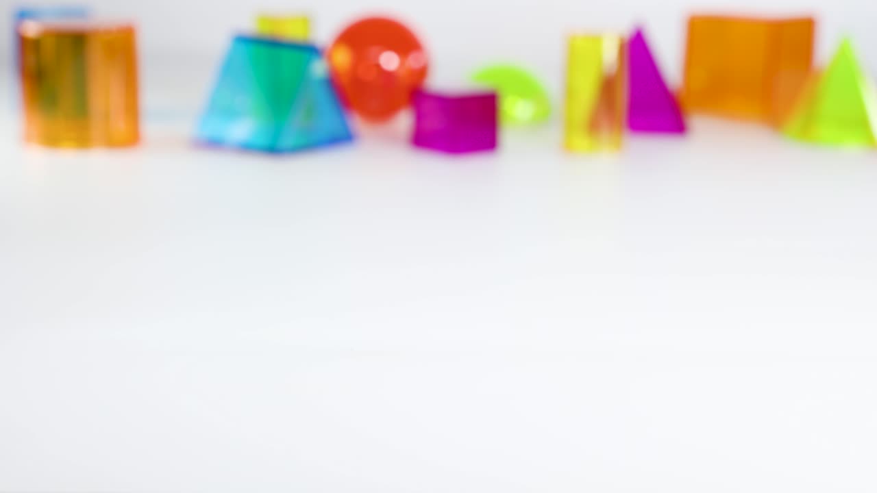 A hand interacts with a blue cuboid among various colorful geometric shapes on a white surface