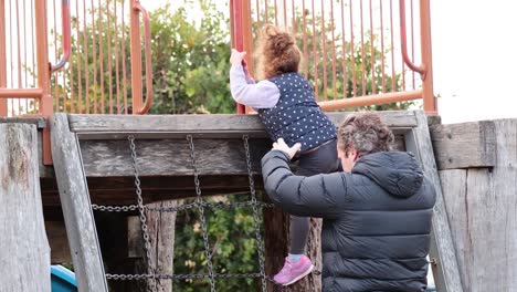 adult helps child climb wooden structure