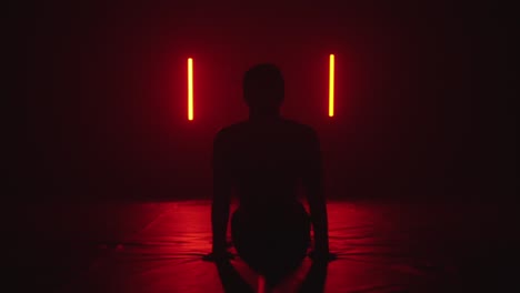 man practicing yoga in dark room, red lights casting shadow silhouette