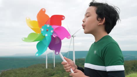 progressive young asian boy playing with wind turbine toy at wind turbine farm.