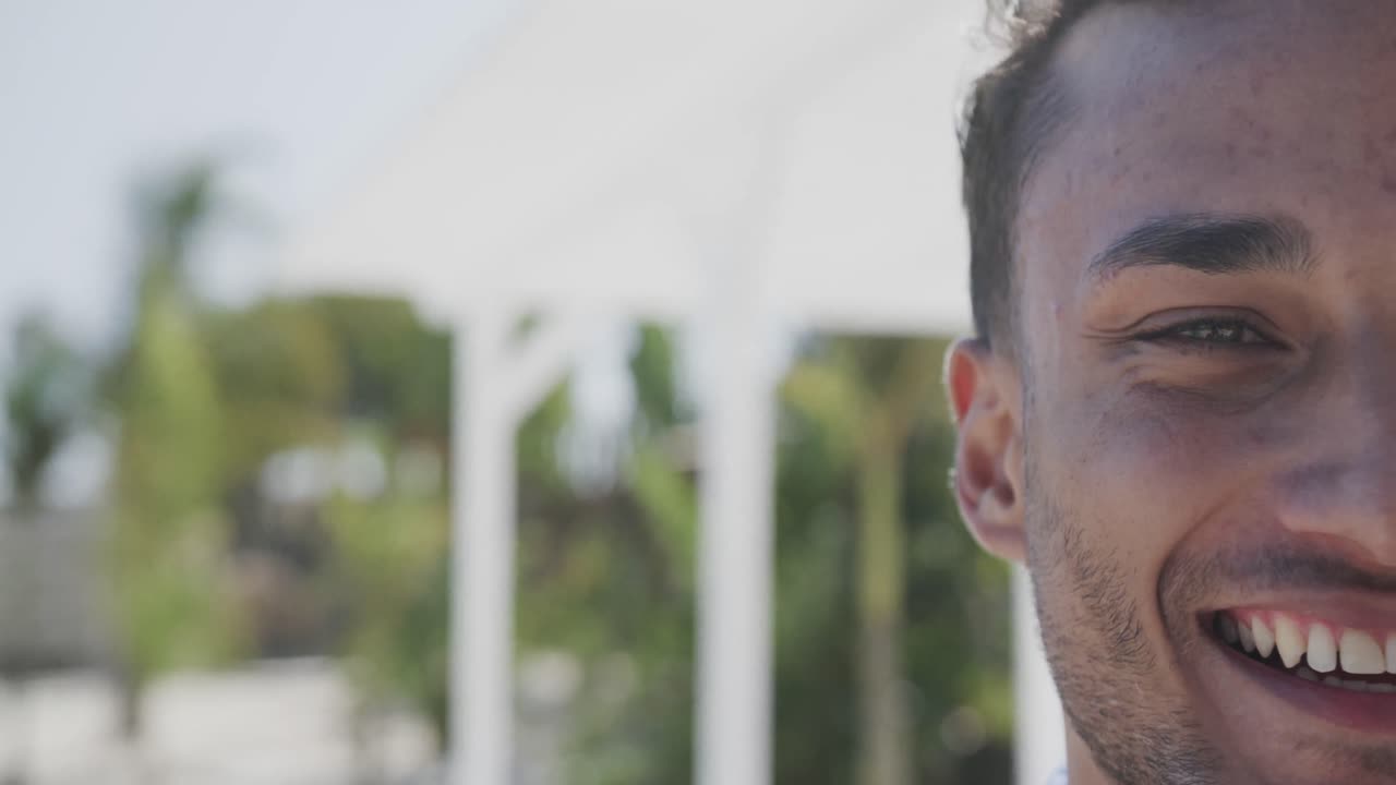 Medio retrato de hombre birracial feliz sonriendo en una playa soleada, en cámara lenta con espacio para texto