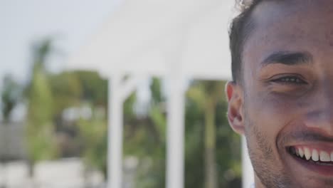 Half-portrait-of-happy-biracial-man-smiling-on-sunny-beach,-in-slow-motion-with-copy-space