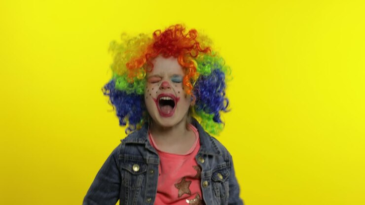 Bambina clown arrabbiata con parrucca colorata che fa facce cattive. Mostra il pugno. Halloween. Espressioni.