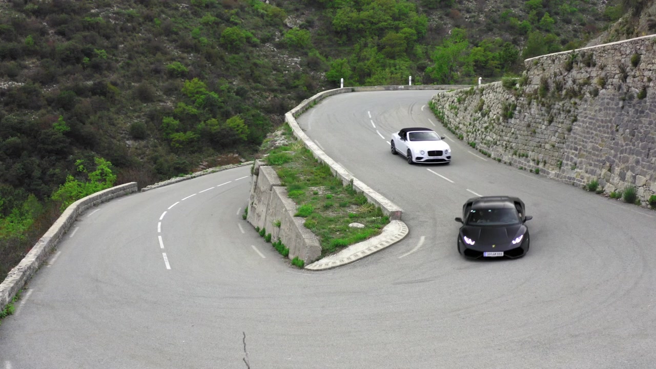 Auto sportiva Lamborghini seguita da Bentley che percorrono le curve nelle Alpi, riprese da drone.