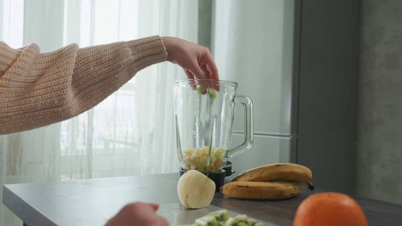 Preparare la frutta per un frullato a colazione in cucina. Una persona unisce i frutti nel frullatore per una bevanda mattutina veloce. Routine mattutina casuale di assemblare banane e arance nel frullatore per la colazione.