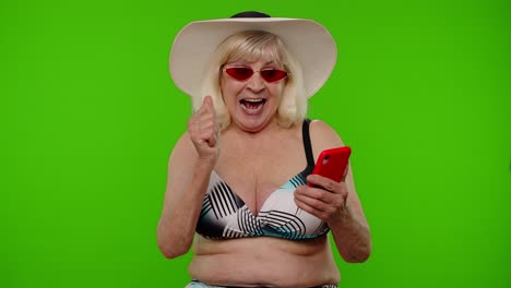mujer madura viajera navegando en el teléfono móvil y celebrando ganando vacaciones en el complejo turístico