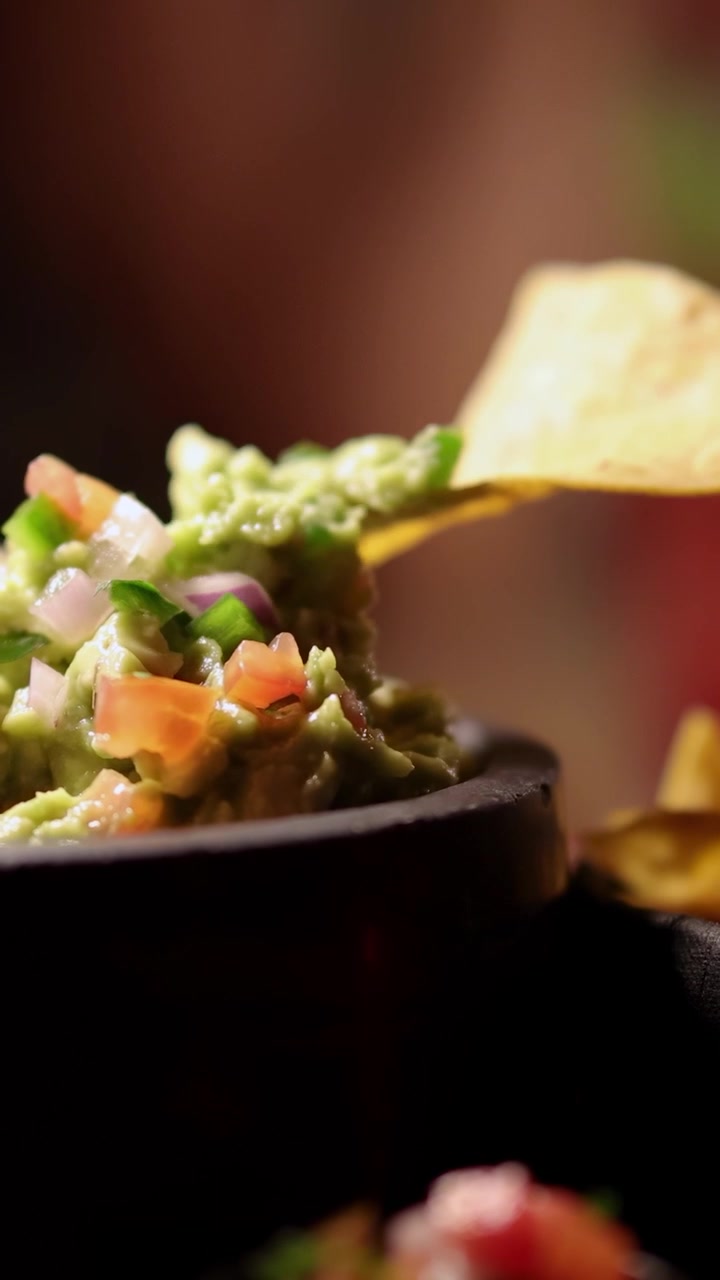 Una mano intinge un nacho in guacamole vivace in un ambiente caldo e accogliente con illuminazione soffusa