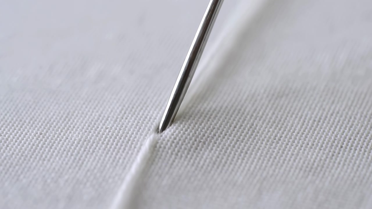 Closeup Needle Piercing White Cotton Fabric, Shiny Steel Needle Pushing Along Seam Line On Textured Woven