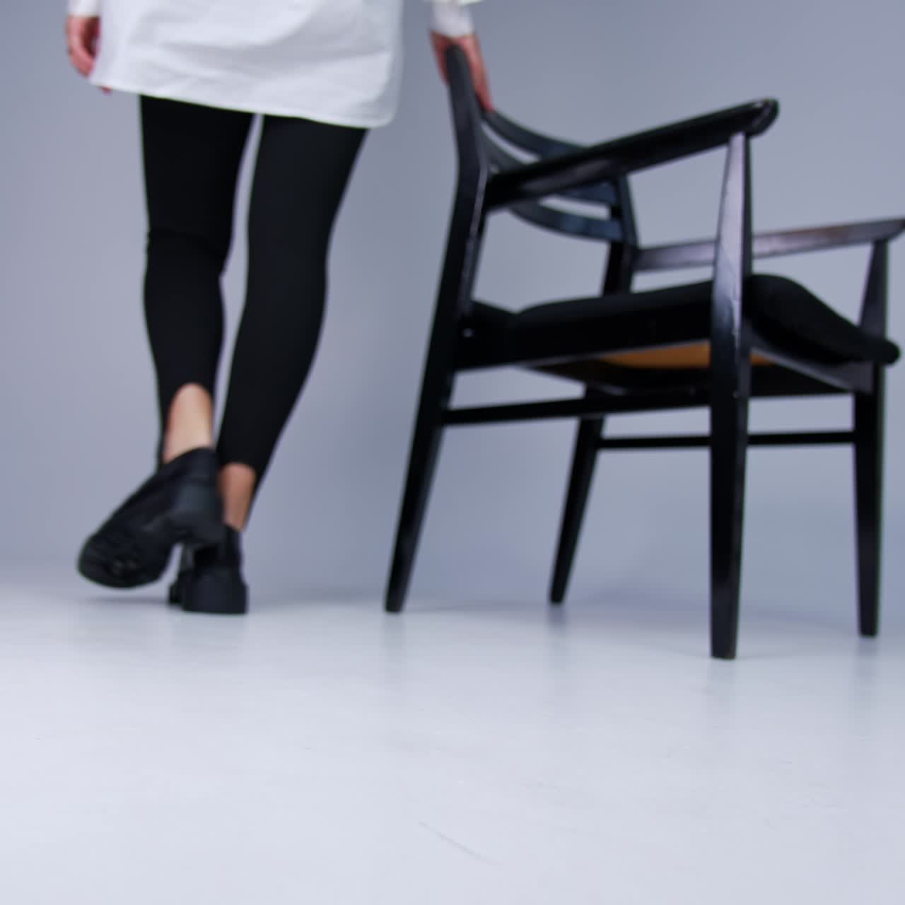 Female model demonstrating stylish shoes on thick tractor soles. White studio backdrop with black chair at backdrop