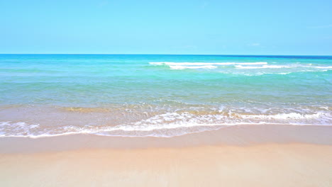 foamy turquoise waves rolling over white sand beach in thailand on idyllic sunny day