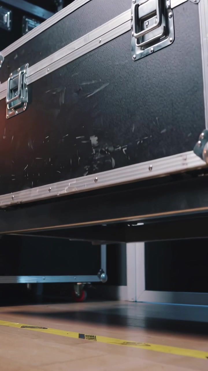 Vertical video: Rolling black road case after dolly rolling across venue floor, passing yellow tape