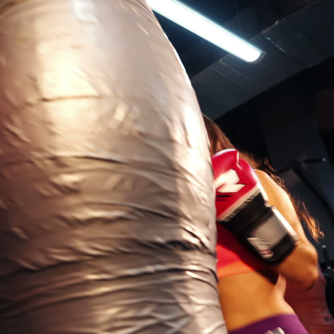 Attractive brunette with long hair boxing pear on the background of sports centre. Fitness girl in boxing gloves and sportswear beating pear. Close-up