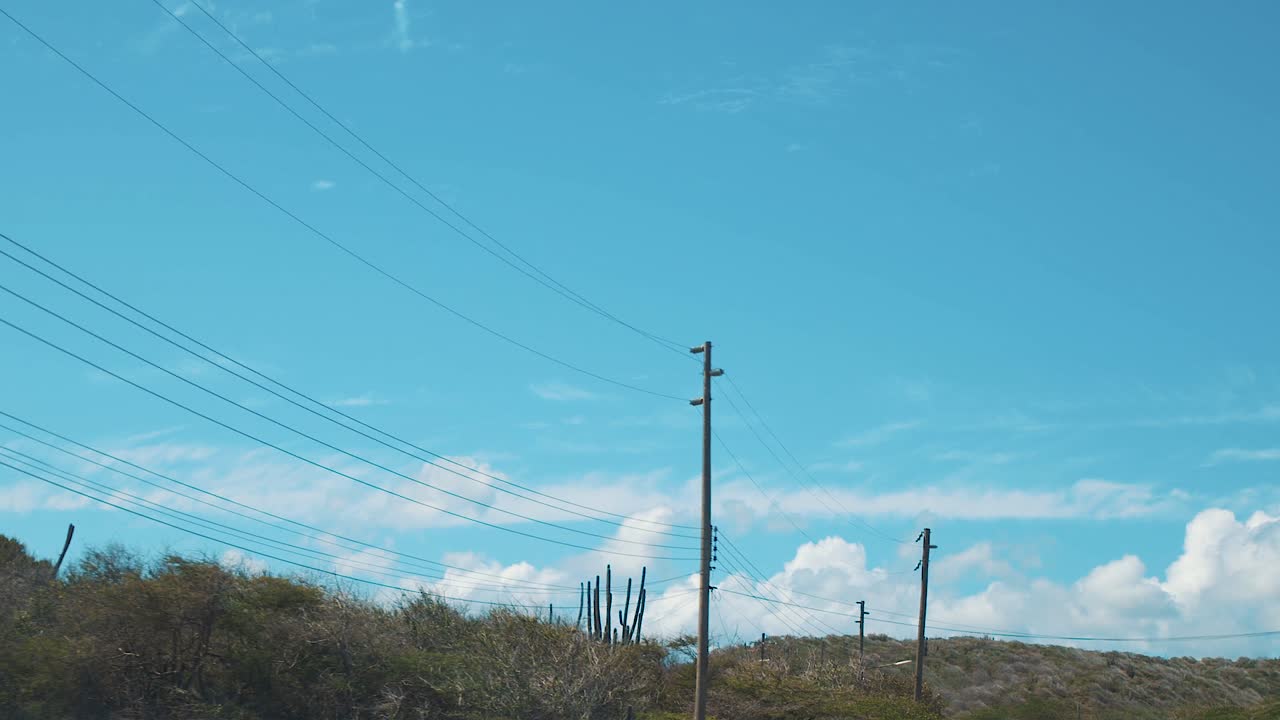 Curacao - Electrical Poles With Cables Attached Along The Street With Green Trees Under The Blue Sky - Panoramic Shot
