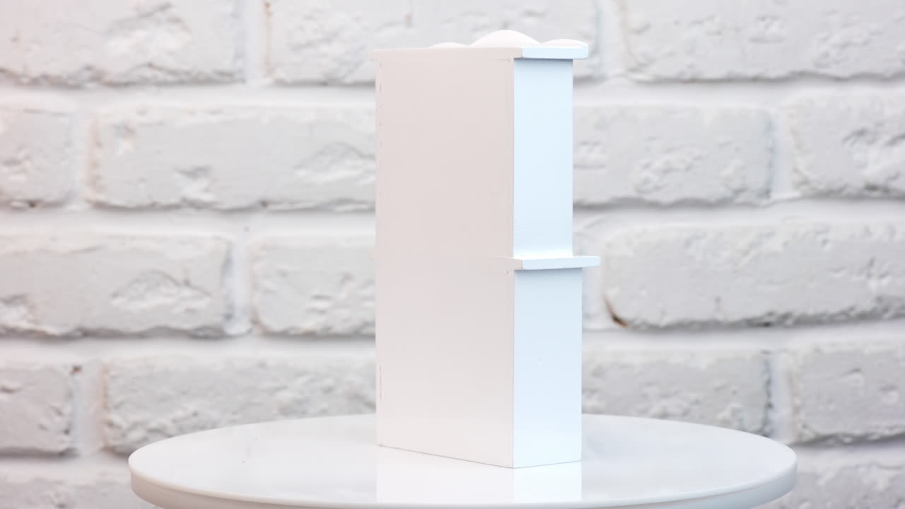 Cute white wooden cupboard rotating on the table. Little toy furniture close up at white backdrop.