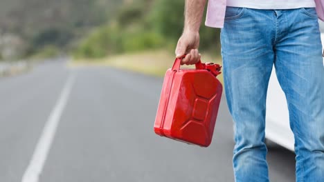 sección media de un hombre caucásico caminando en una carretera rural llevando combustible jerrycan