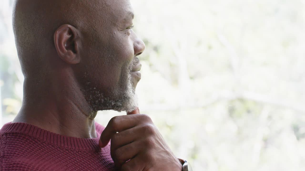 Thoughtful african american senior man looking out window at home, slow motion