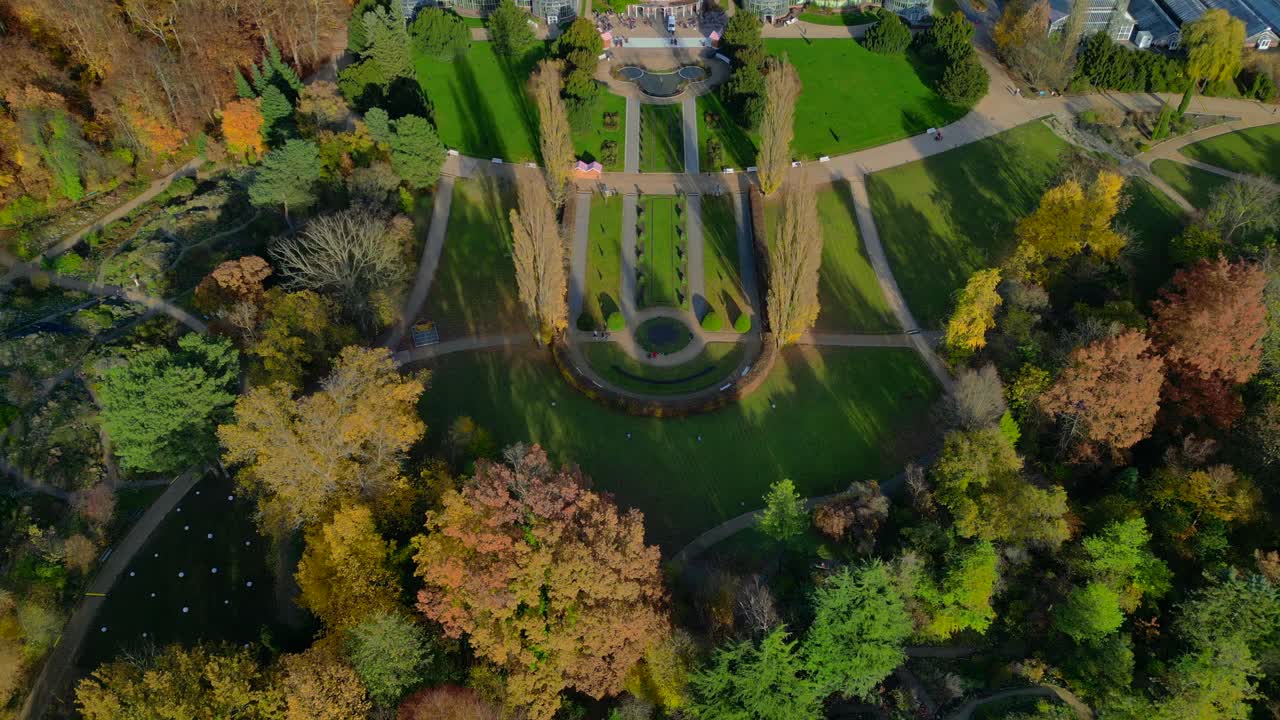 Botanical Garden Berlin 100-year old Victoria House greenhouses surrounded by autumn trees and urban landscape. Majestic aerial view flight tilt up drone