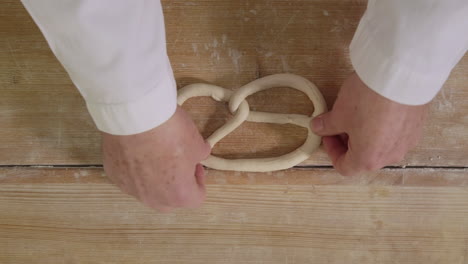 handmade german pretzel formed by baker on wooden table in traditional bakery