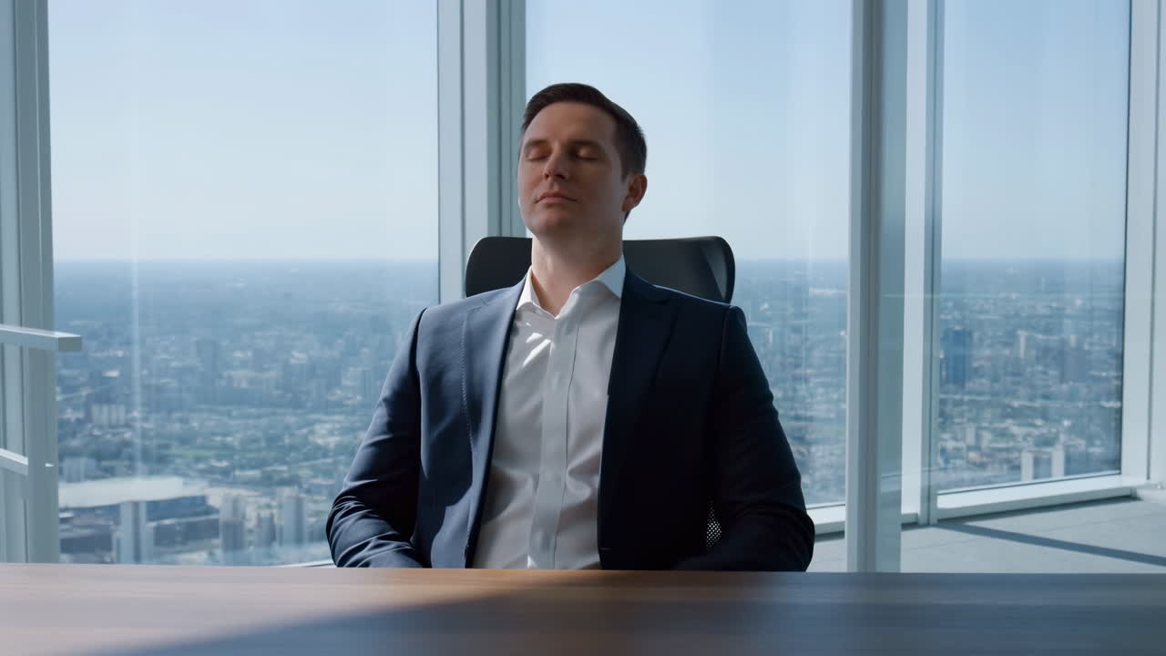 Kaukasisk forretningsmand sidder ved skrivebord med lukkede øjne og tager en mindful pause på et højhus-kontor med udsigt til byens skyline.