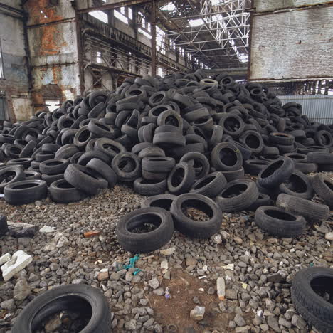 a bunch of car tires are in an abandoned high hangar with holes in the windows of building. view of old factory inside. close-up.