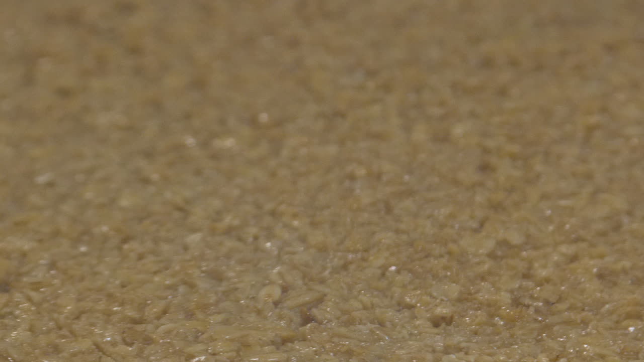 un primer plano extremo de la mezcla de pastel flapjack se corta en rodajas con una hoja robótica a medida que la mezcla se mueve a lo largo del transportador