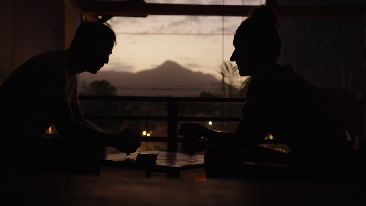 Travelers playing cards in Palomino, Colombia, scenic silhouette dawn moment, mountain top in background, backlight setting