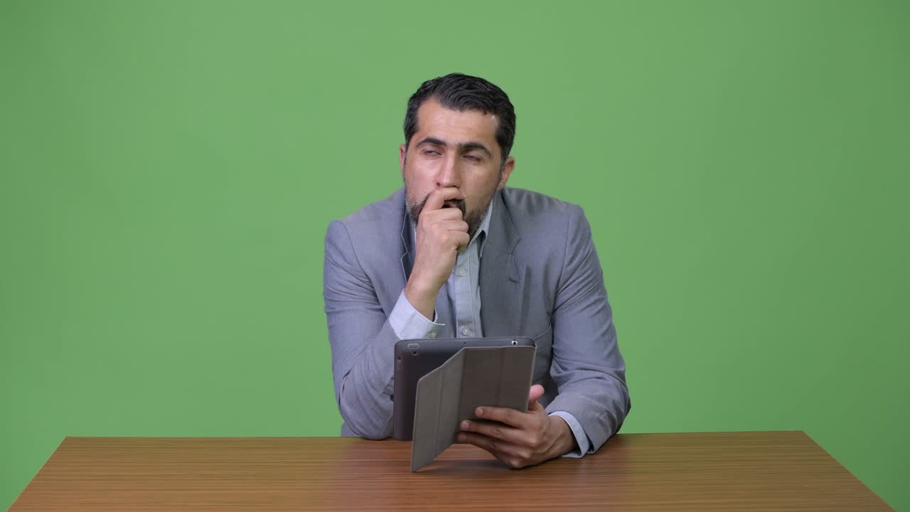 Handsome Persian bearded businessman thinking while using digital tablet