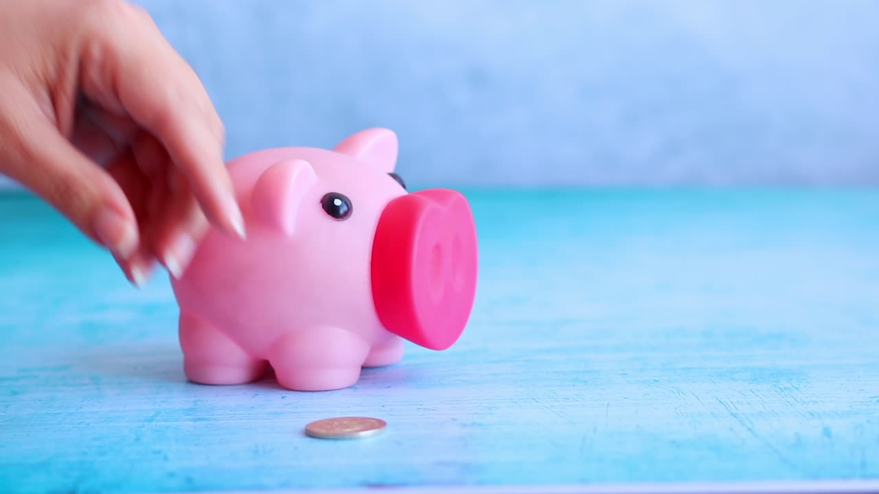 Hand Putting Coins into a Pink Piggy Bank