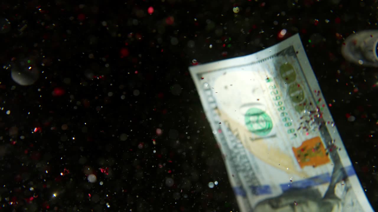 Falling flying american dollar banknotes and flying mixing with the glitter sparkles on a black background in 4K Loopable. High quality falling Dollar banknotes in 4K. Video is Loopable
