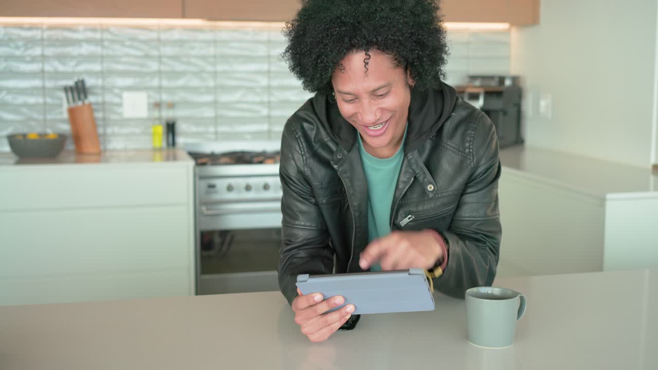 African American man leaning on kitchen island, tapping tablet, smiling and swiping for fun