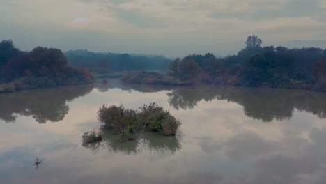 flying above the surface of a clear reflective lake in a forest on an early autumn morning